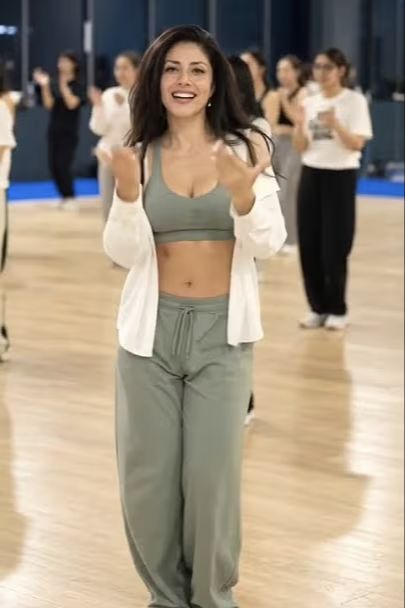 MarGo dancing in a gym studio, wearing a sage outfit and white overshirt.